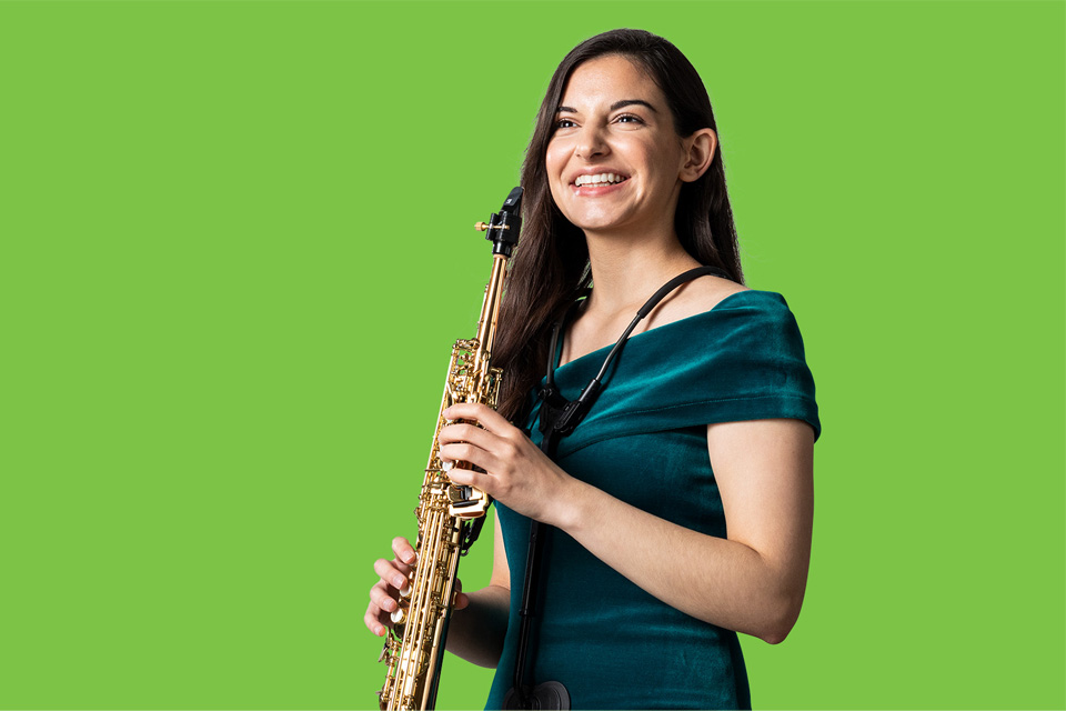 Student in green dress with a soprano saxophone, against a light green background.